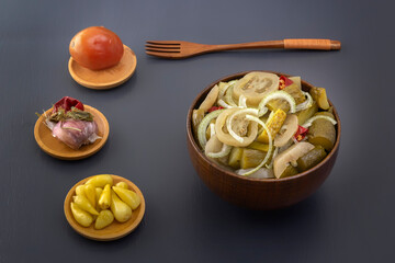 Slicing fermented green tomatoes and cucumbers with onions pickled garlic in a wooden bowl on a gray table.
