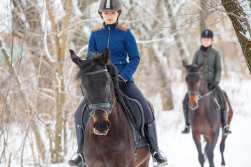 Obraz premium Two girls riding horse in snowy park in winter.