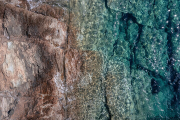 Top-down view of flat coastal cliffs extending into turquoise water with sun flares, Crete, Greece