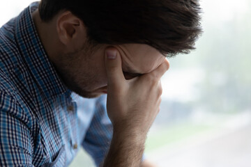 Fototapeta premium Sad hopeless young man sit alone indoor looks desperate, cover face with head suffers, troubled with concerns, divorce or drama feeling unhappy after quarrel or breakup, psychological problem concept