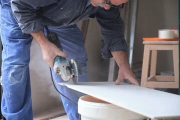 Senior constructor worker cutting a white ceramic tile with a radial saw.