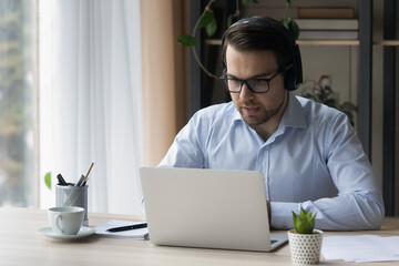 Professional online counselling, support to client virtually use videocall app, modern tech concept. Young man in glasses sit at desk wear headset take part in briefing by video conference on computer