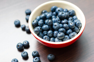Blueberries in a red bowl on wooden table.