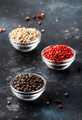 Black, white and pink rose peppers in glass bowls, assorted spices on kitchen table, copy space
