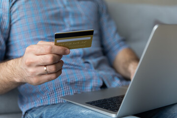 Secure e-bank system to prevent scam, client of e-commerce, electronic services make purchase online concept. Cropped close up image man sit on sofa with laptop holds credit card buying on internet