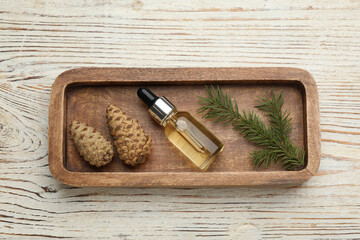 Fototapeta na wymiar Tray with bottle of essential oil, fir branch and cones on white wooden table, top view