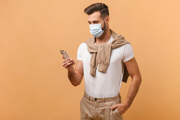 Portrait of concentrated man in protective mask using smartphone, while reading something, enjoying mobile application. Man looking at the device screen
