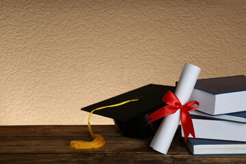 Graduation hat, books and diploma on wooden table. Space for text