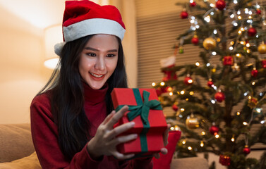 An Asian woman alone in a room. Opening a box of gifts received from boyfriends, friends or family with a surprise during Christmas. Christmas and long distance relationship concept.