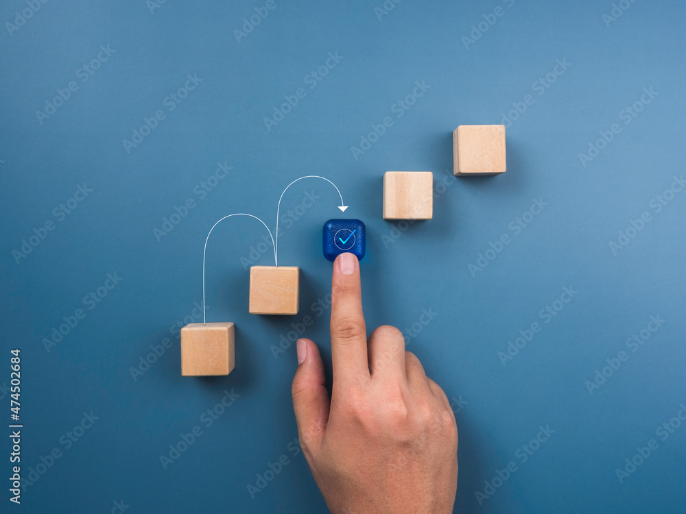Aufkleber solution concept. the checkmark icon on a blue cube is placed by hand as a bridge between wooden blo