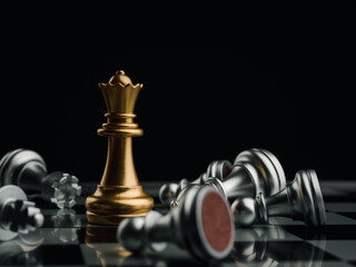 Close-up golden queen chess piece standing with falling silver pawn chess pieces on chessboard on...