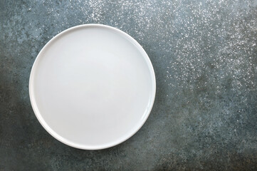 Empty white plate on a gray-blue background sprinkled with powder.