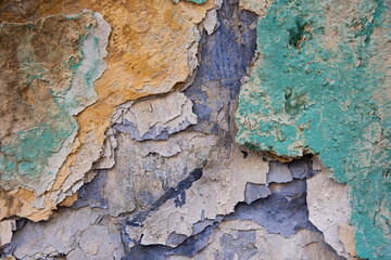 Multi-colored layers of cracked and peeling paint on stonework and walls of old buildings.