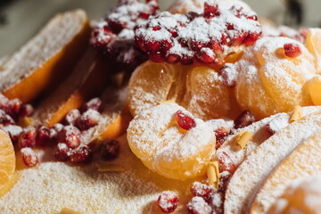 Close up decor of Christmas cake decorated with tangerines, pomegranate and powdered sugar. Traditional Christmas cake decorated with glaze, pomegranate seeds. Selective focus