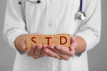 Doctor holding wooden cubes with abbreviation STD on grey background, closeup