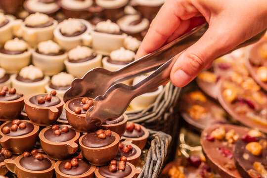 Chocolate store, unrecognizable hand holding a food clip picking up a chocolate bonbon, selective focus on the bonbon