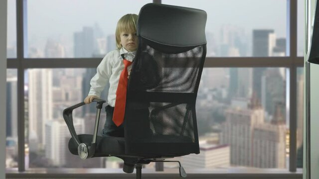 Shy and spoiled child with red tie on businessman armchair, window panorama