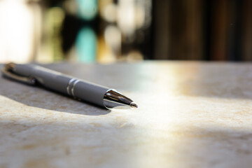 The ballpoint pen is on the table. Solar lighting. Blurred background - books.