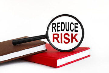 REDUCE RISK. white background text on magnifying glass. magnifying glass on brown and red notebook