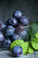 Fresh plums in a glass vase with green leaves. Summer still life.