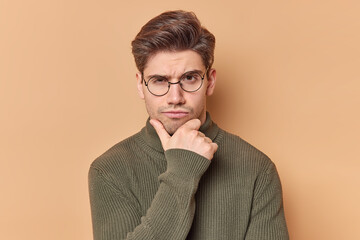 Portrait of serious skeptic man holds chin looks attentively at camera feels self confident...