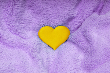 a bright yellow heart on a crumpled purple plush blanket; a concept for the design of valentines and other greeting cards related to love
