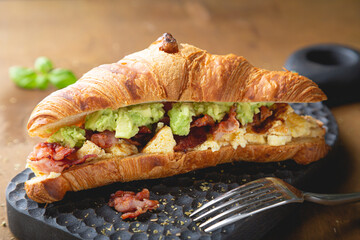 Croissant breakfast sandwich with scrambled eggs, bacon and avocado