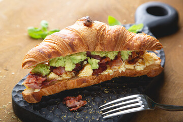 Croissant breakfast sandwich with scrambled eggs, bacon and avocado