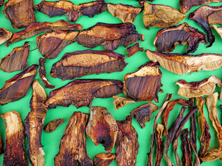 Dried flat layer of sliced boletus mushroom covering whole frame on green background.
