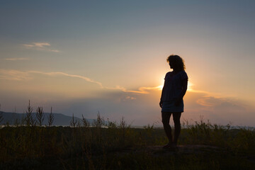 Fototapeta premium Silhouette of a young woman against the sky. Summer sunset.
