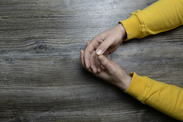 Men's hands in a yellow jacket lie on a gray wooden surface, which is used as a background or a surface with incident light.