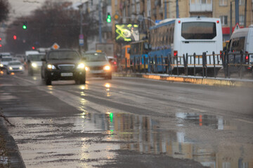 Cars on the road with puddles at snowy evening