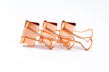 Three shiny paper clips in rose gold metal on white background. Office or paper desk supplies concept.