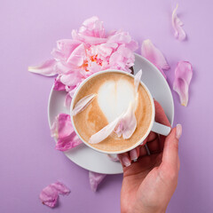 Female hands holding a cup of coffee. Blouse with romantic pink background and rose petals.