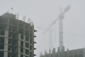 High-rise cranes next to buildings under construction. Kyiv, Ukraine. Fog in the city.