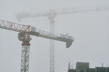 High-rise cranes next to buildings under construction. Kyiv, Ukraine. Fog in the city.