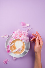 Female hands holding a cup of coffee. Blouse with romantic pink background and rose petals.