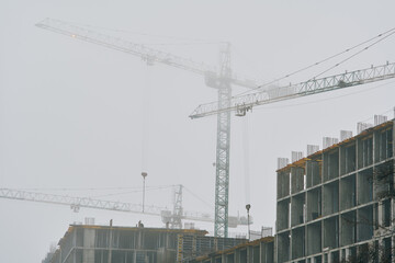 High-rise cranes next to buildings under construction. Kyiv, Ukraine. Fog in the city.