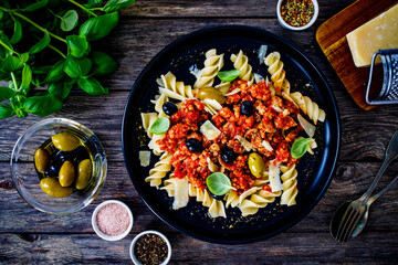Fusilli with minced meat, tomato sauce, parmesan cheese and olives served on wooden table
