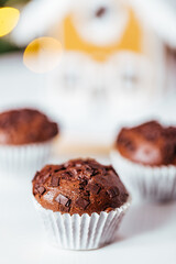 Chocolate cupcakes or muffins with Ginger house and Christmas lights from Christmas tree in blurry background. Festive and holiday decoration