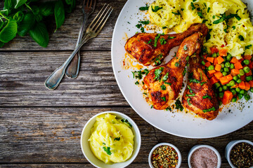 Barbecue chicken drumsticks with potato puree, grean peas and carrot on wooden table
