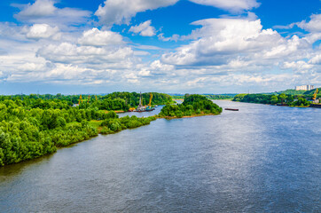 Summer landscape with river, green hill and warm blue cloudy sky. There is a small port on the shore with loading cranes.