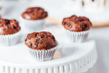 Chocolate cupcakes or muffins with Ginger house and Christmas lights from Christmas tree in blurry background. Festive and holiday decoration