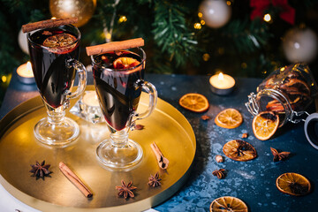 Fototapeta na wymiar Mulled wine with cinnamon, anise star and orange served in festive Christmas decoration in front of a Christmas tree and lights. Ideal drink for advent and celebration.