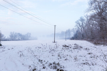 Winter landscape with power line, clearing in the forest covered with snow on a foggy day