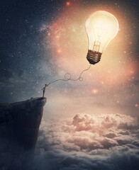 Creative idea concept with a person on the edge of a cliff holding the string of a lightbulb kite...