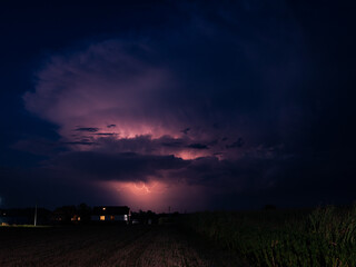 Naklejka na ściany i meble Evening thundercloud over the Romanian landscape is illuminated by pink lightning