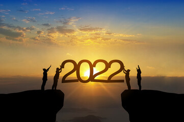 Silhouette of happy teamwork standing and touch 2022 text on beautiful sunrise background celebrate...
