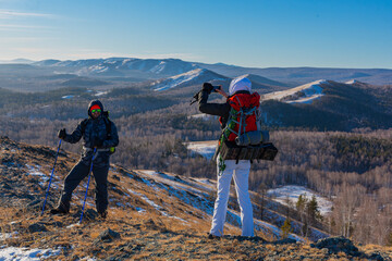 Middle-aged couple go hiking in the alpine winter mountains at dawn - they make a photo with...