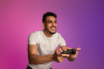 Happy young Arab guy with joystick playing video game in neon light. Modern hobbies concept